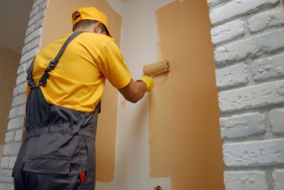 Worker painting wall with paint roller. Builder paints the wall in brown color. Building, renovation and people concept.